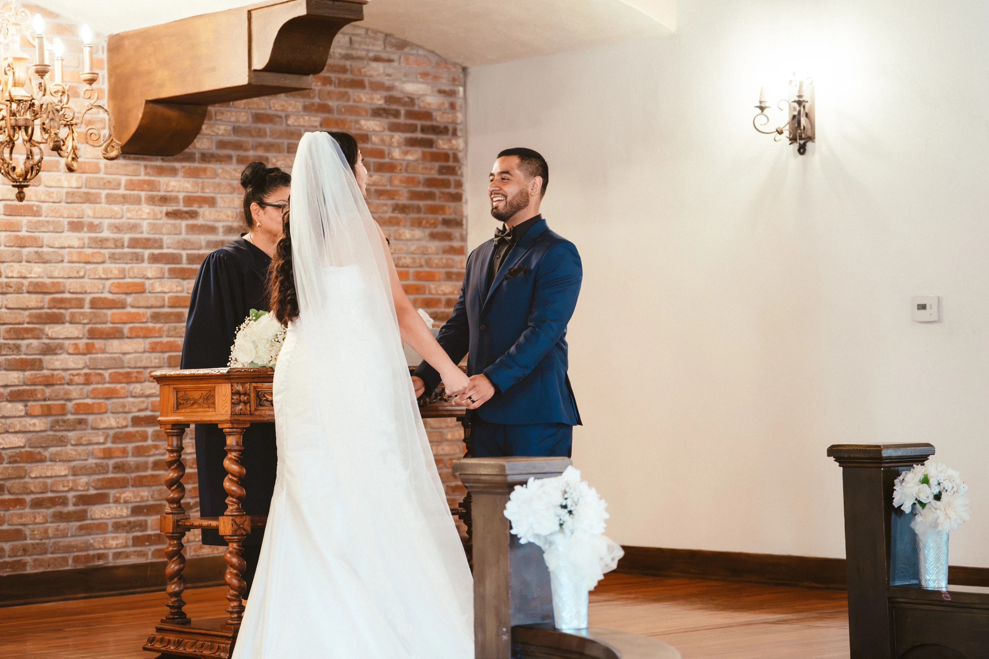 Los novios se toman de las manos en el altar mientras el oficiante lee, y el novio ríe