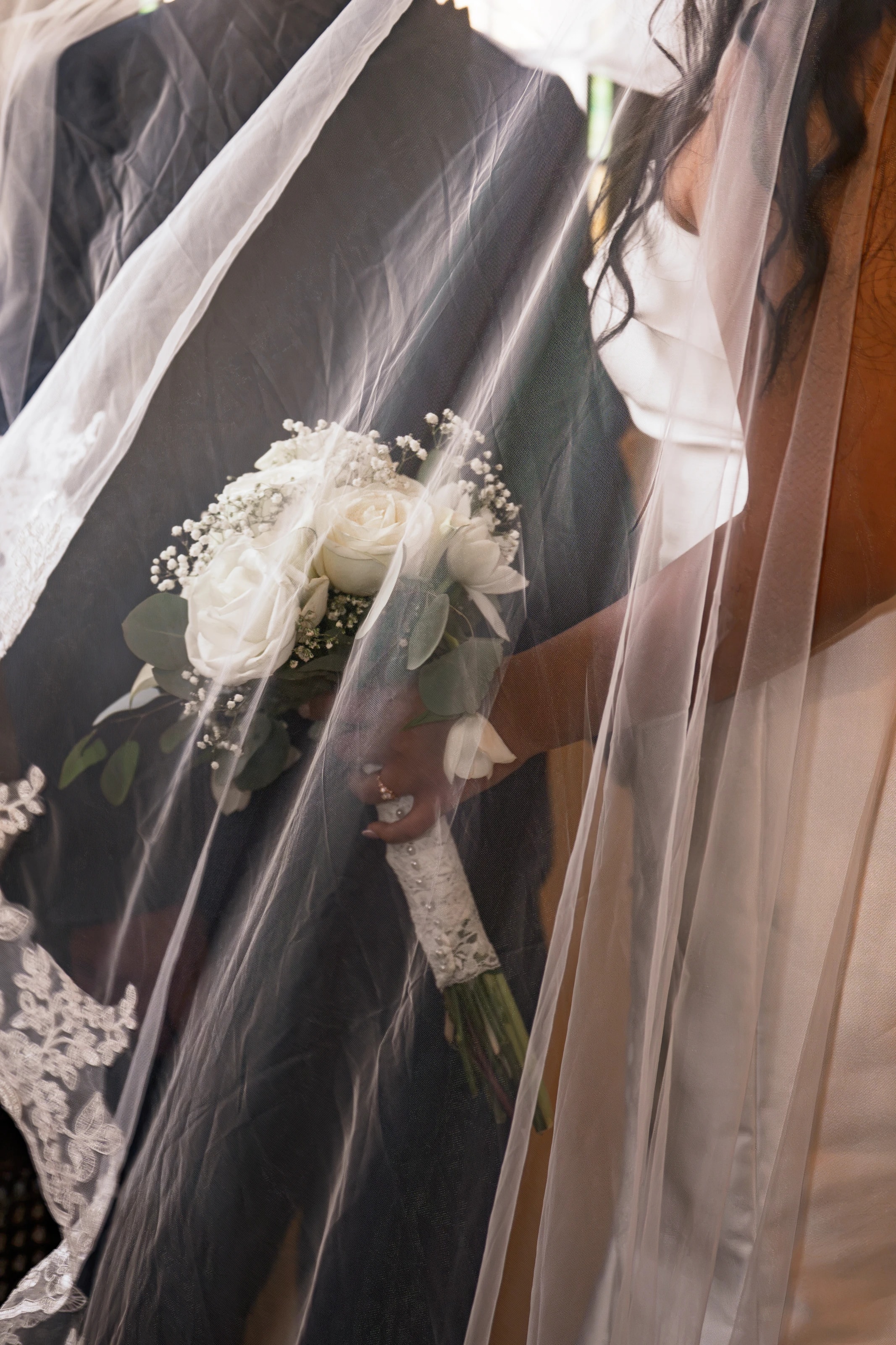 El ramo de rosas blancas de la novia visto a través del velo