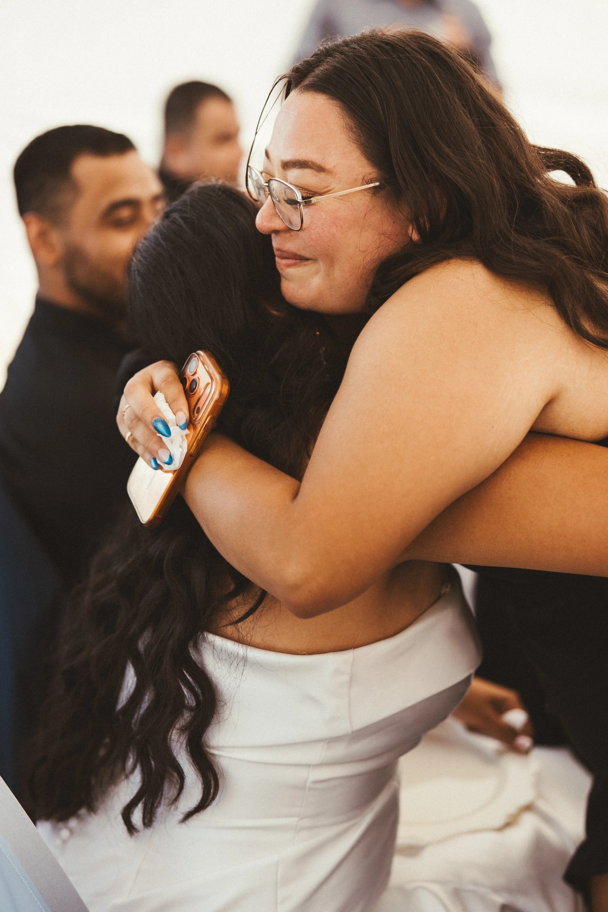 Una invitada abraza con fuerza a la novia, con los ojos cerrados y sonriendo
