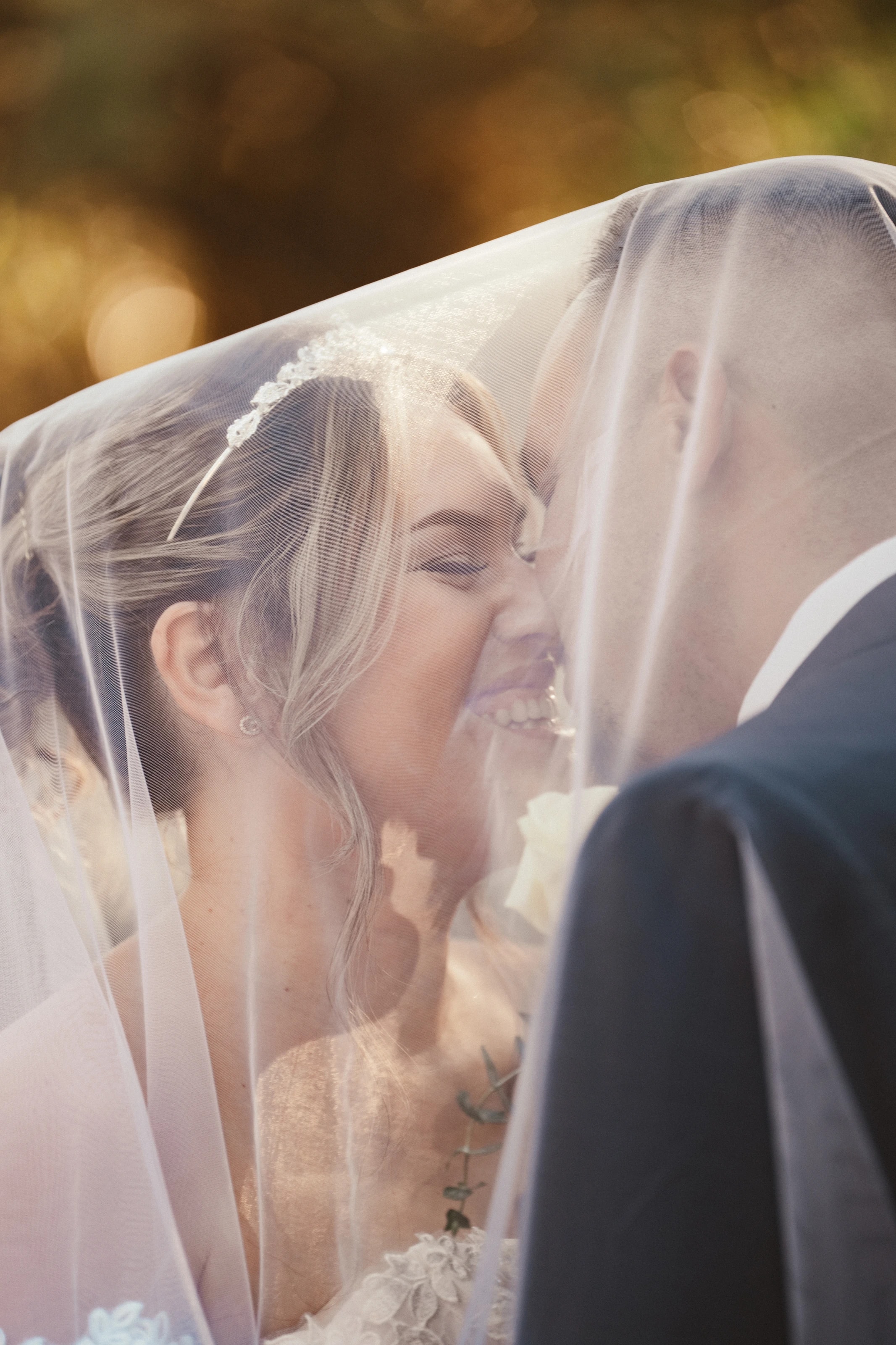 Los novios ríen nariz con nariz bajo el velo, con luz dorada