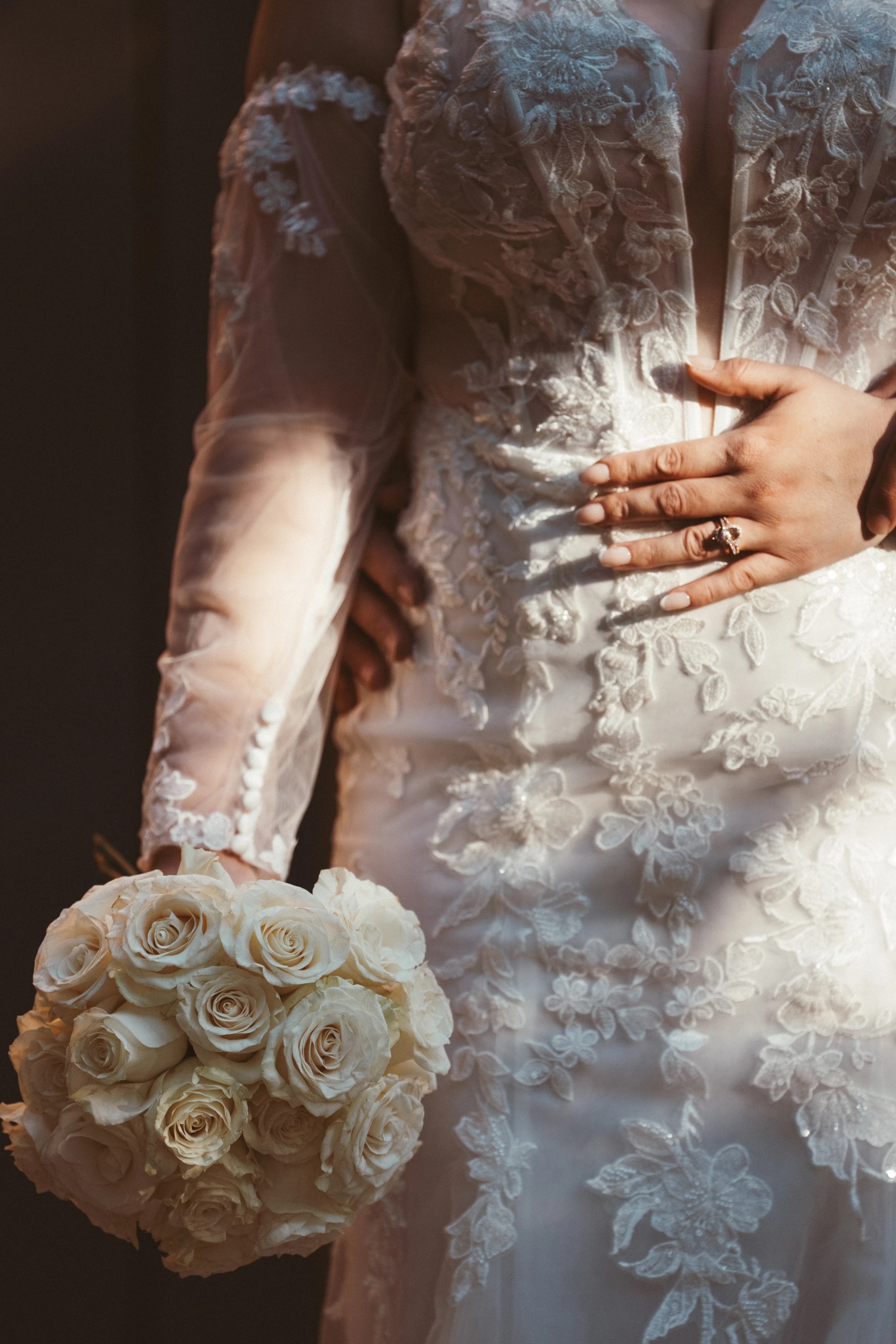 Su mano y su anillo descansan sobre el encaje del vestido junto al ramo