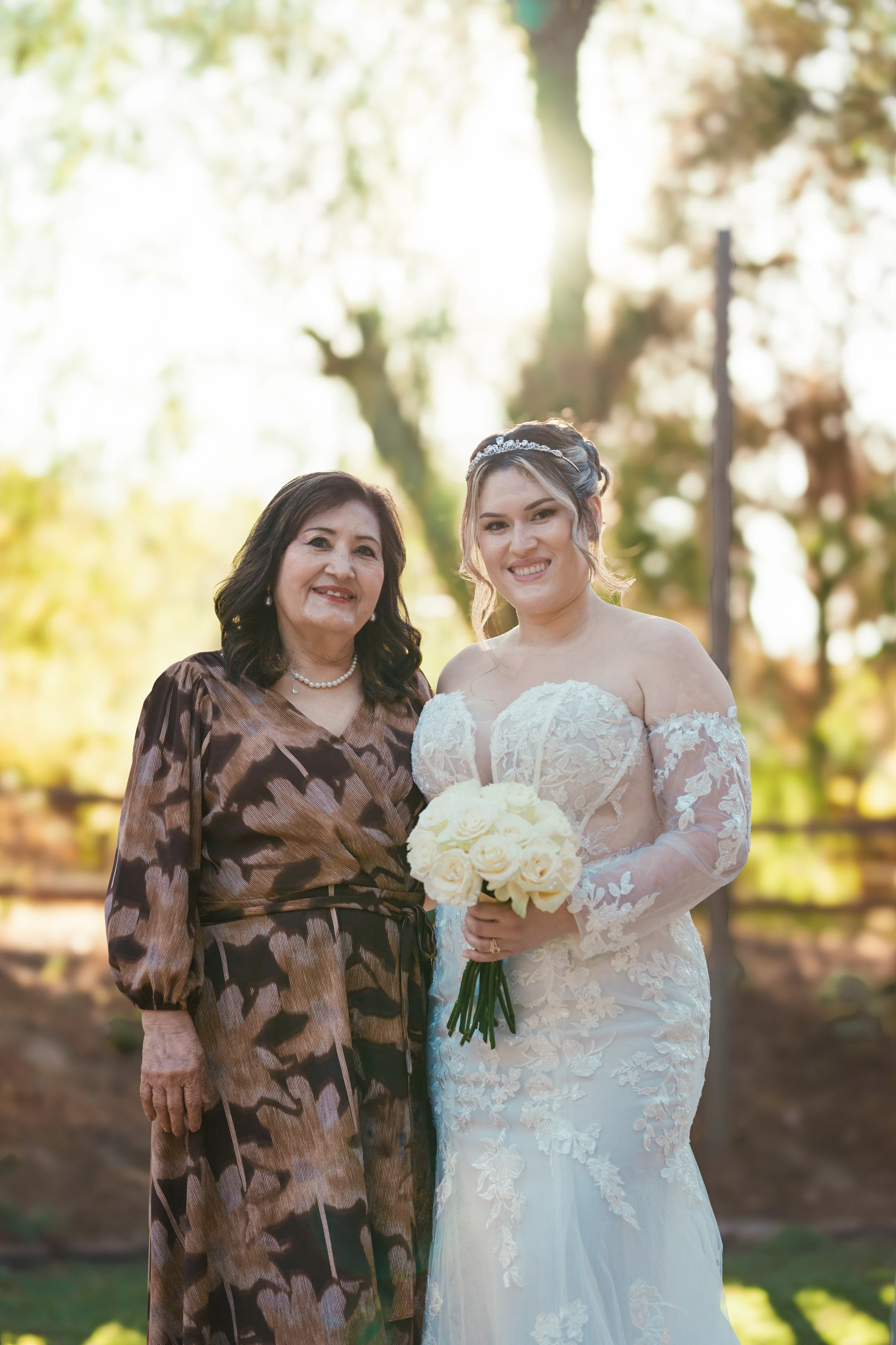 La novia posa con una familiar frente a los árboles iluminados por el sol