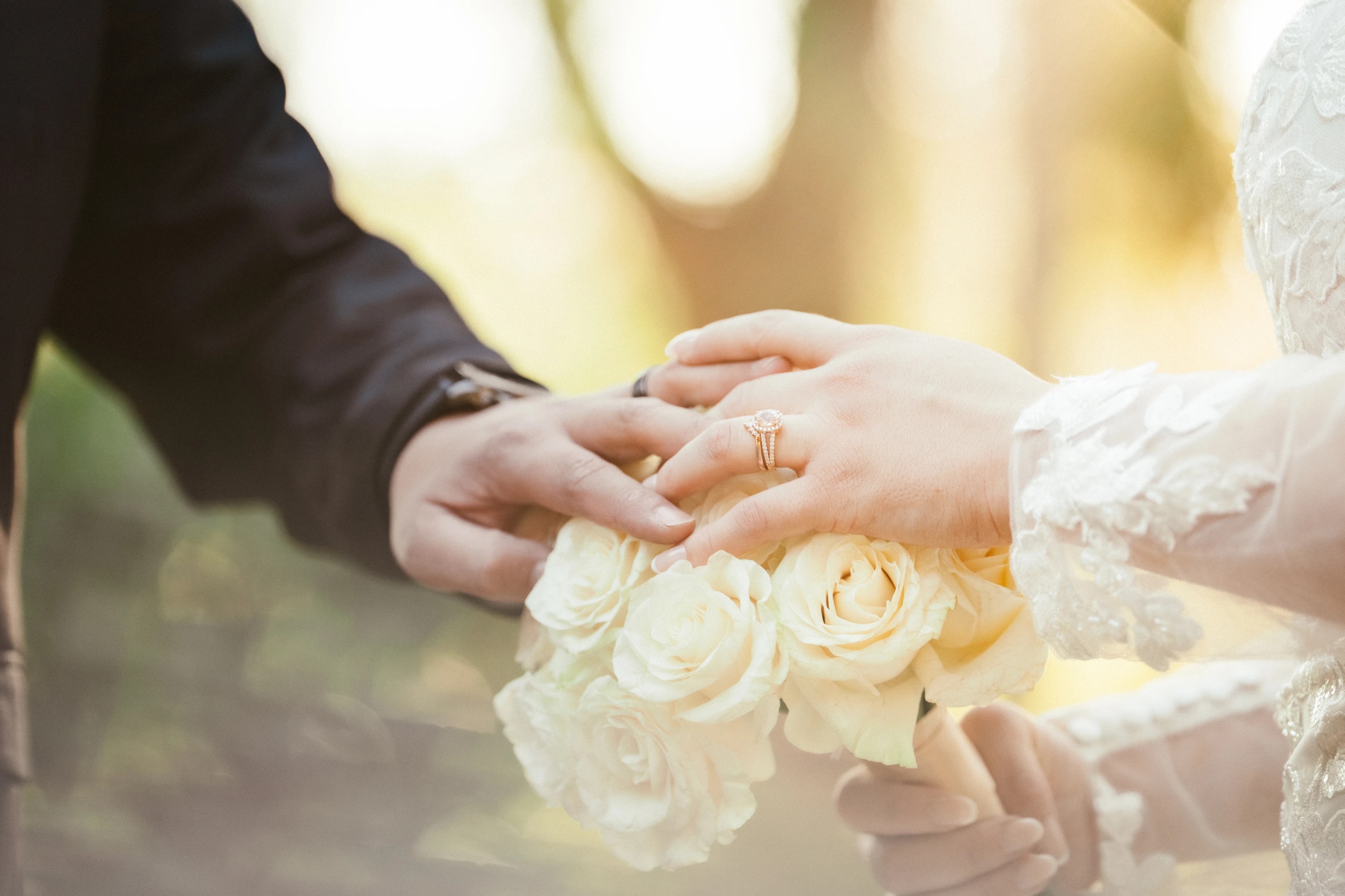 Las manos y los anillos de los novios sobre el ramo de rosas blancas