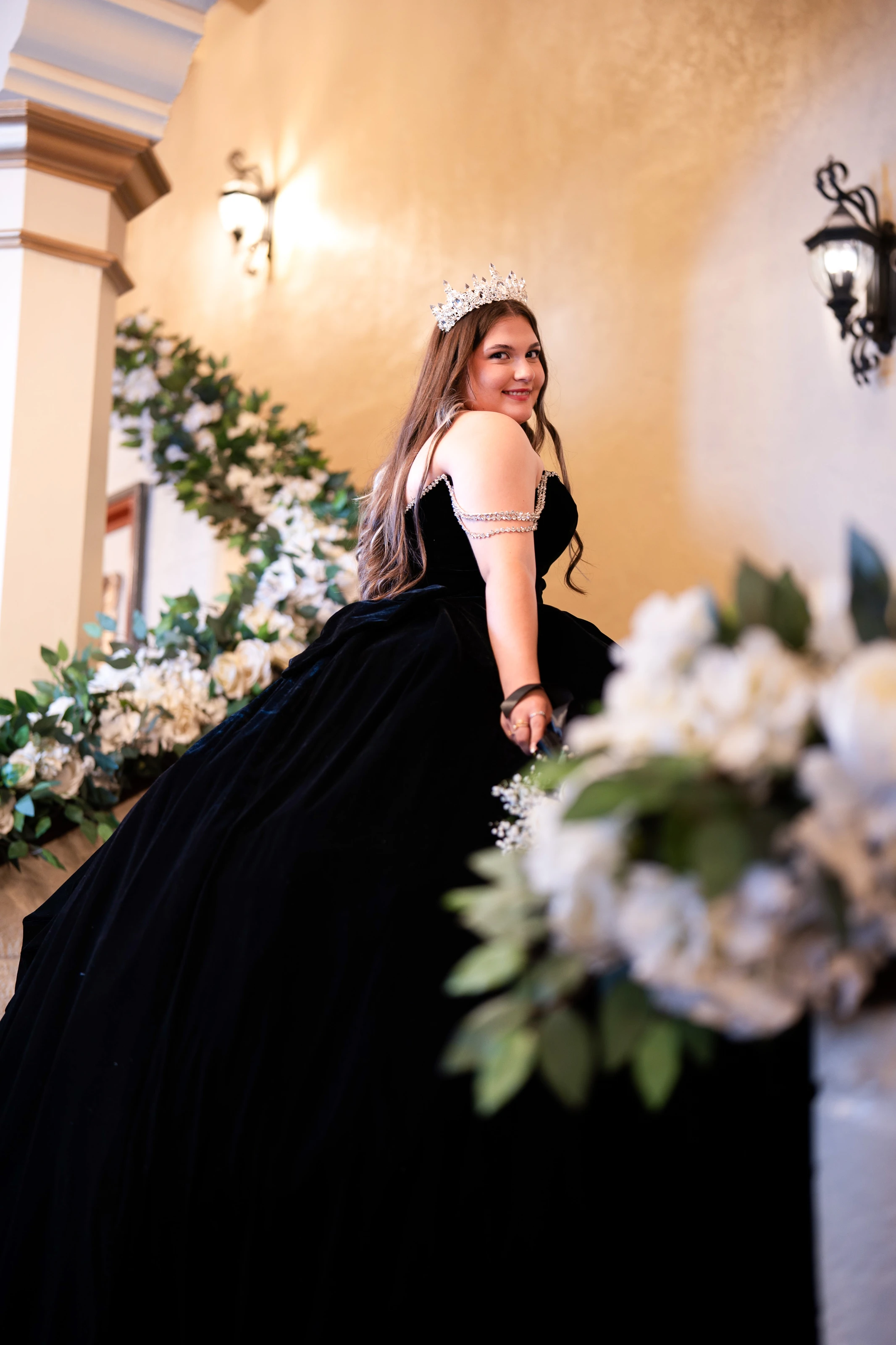 In her black gown, she poses on a staircase lined with white flowers