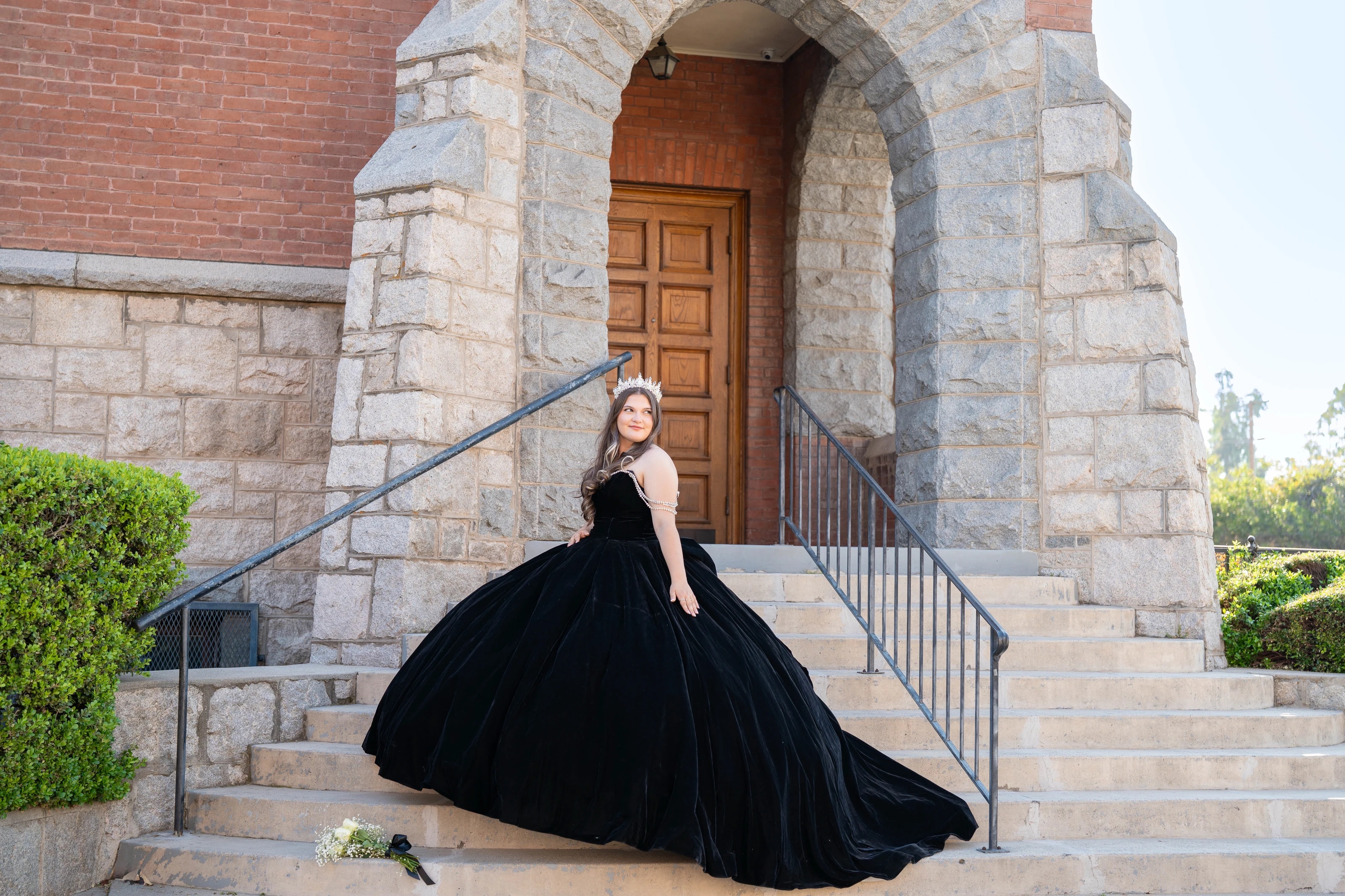 In a black velvet gown, she sits on the steps of a stone church